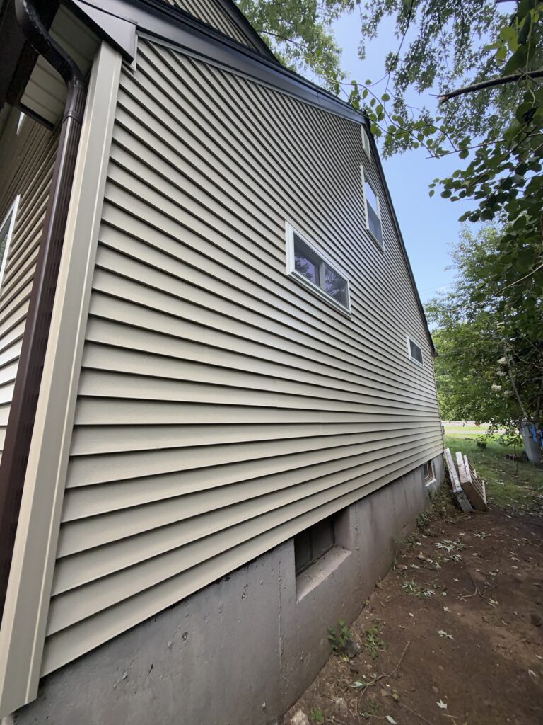 After: new beige vinyl siding and white-trimmed windows, side view, Bristol CT